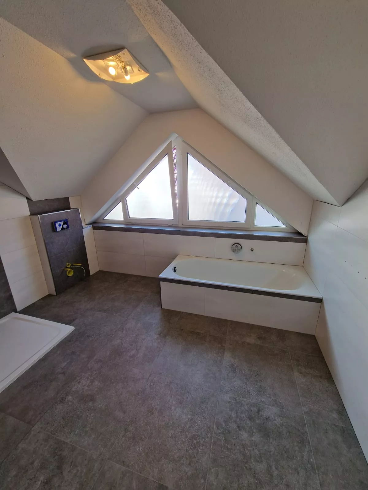 Dachgeschoss-Badezimmer mit Dreiecksfenster, Badewanne und Betonoptik-Boden