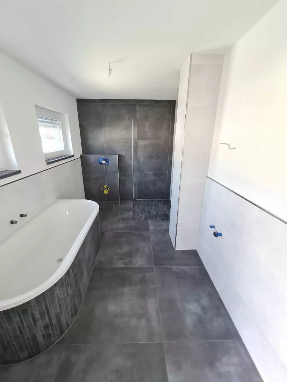 Badezimmer mit halbfreistehender Badewanne, offener Dusche und dunklem Boden