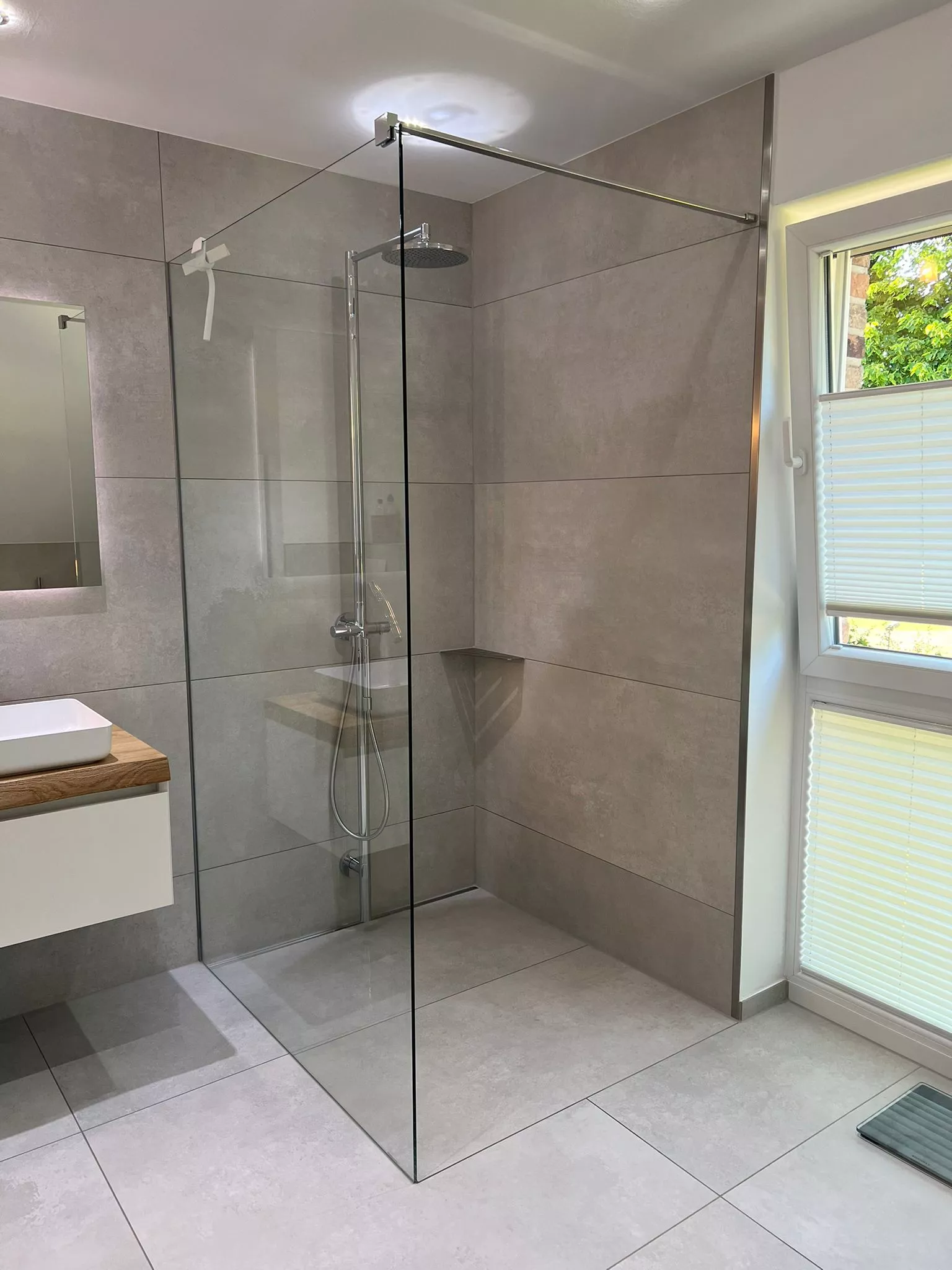 Walk-in-Dusche mit Glaswand, grauen Betonoptik-Fliesen und Regendusche