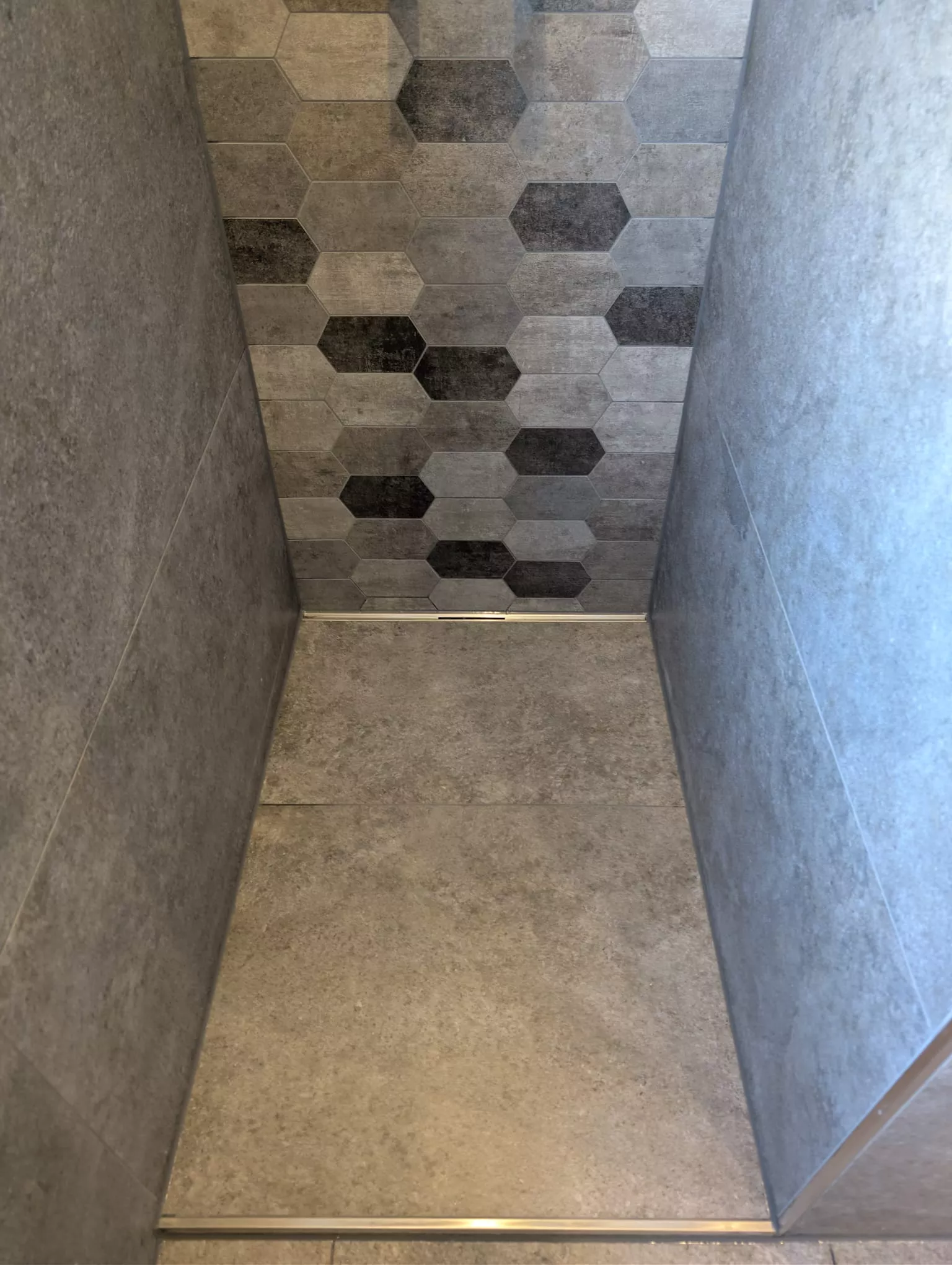 Duschnische mit grau-schwarzen Hexagon-Wandfliesen und Betonoptik-Boden