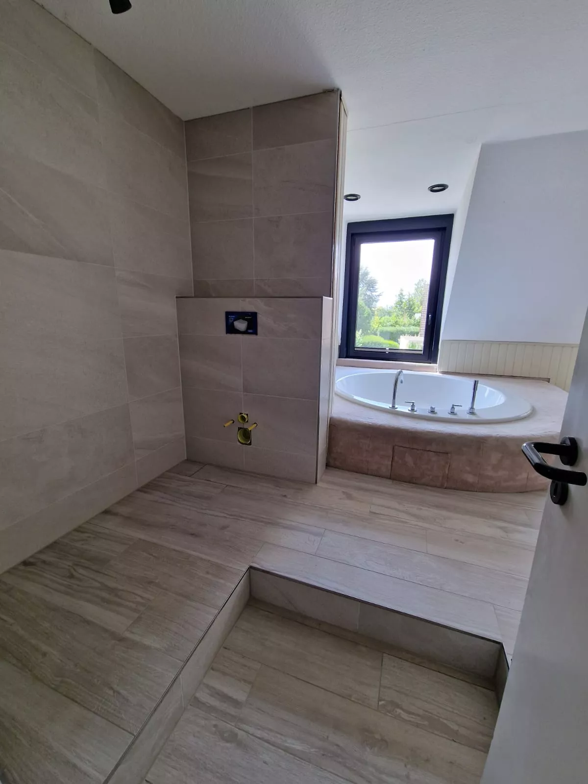 Badezimmer mit Eck-Whirlpool am Fenster, Holzoptik-Boden und Naturstein-Wandfliesen
